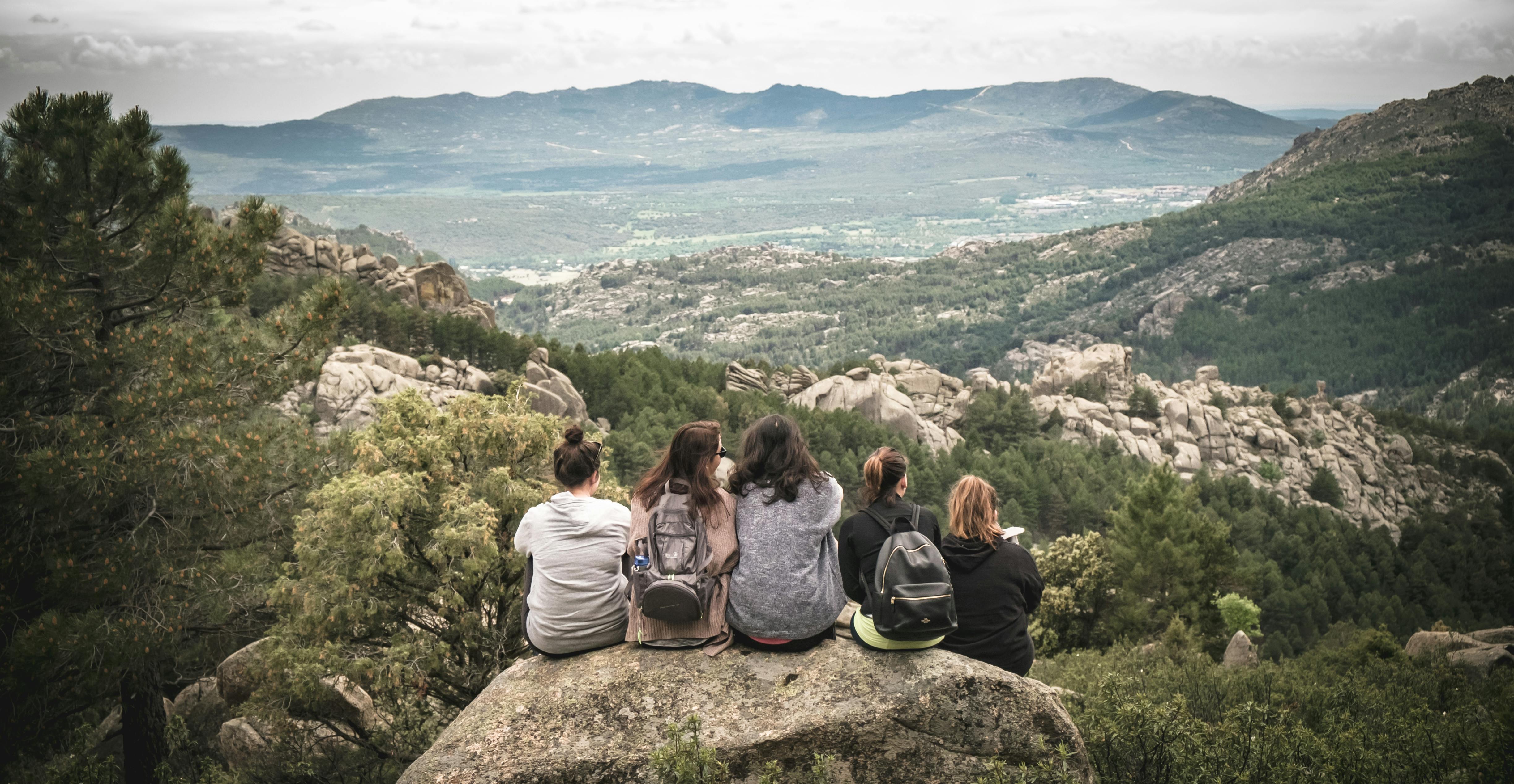 Five women sitting on a rock with their backs to the viewer looking out into the open landscape.