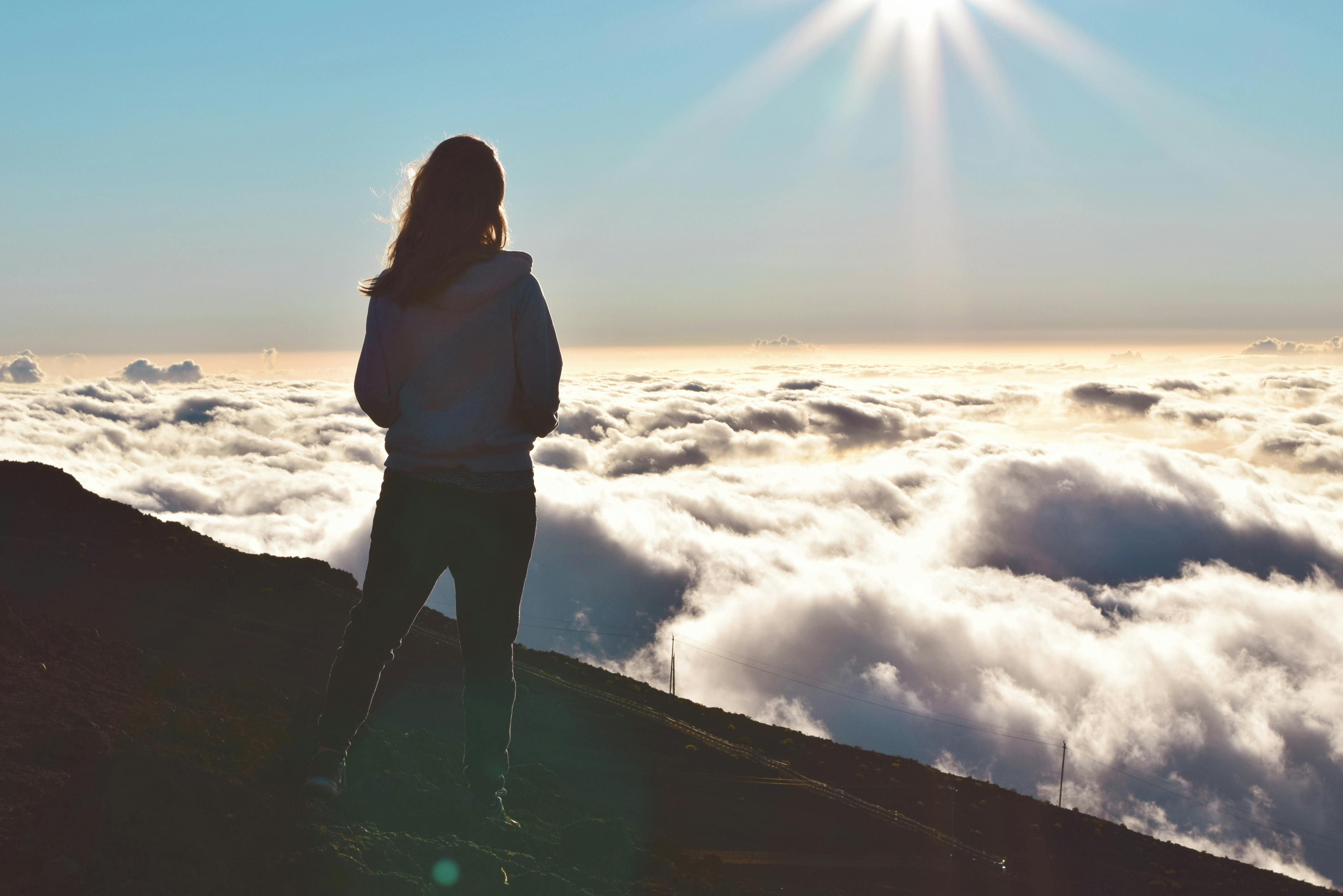 Silhouette of a woman standing on a mountain looking down at a field of clouds